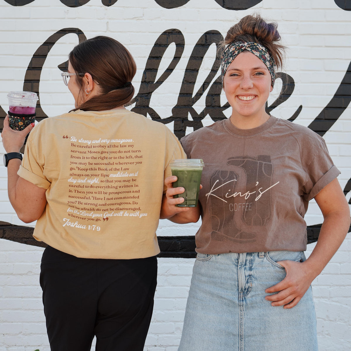 Two people standing in front of a wall with 'Kino's Coffee' written on it, holding drinks.